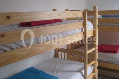 Lit double avec une couette blanche dans une chambre mansardée aux murs en pierre et plafond en bois.