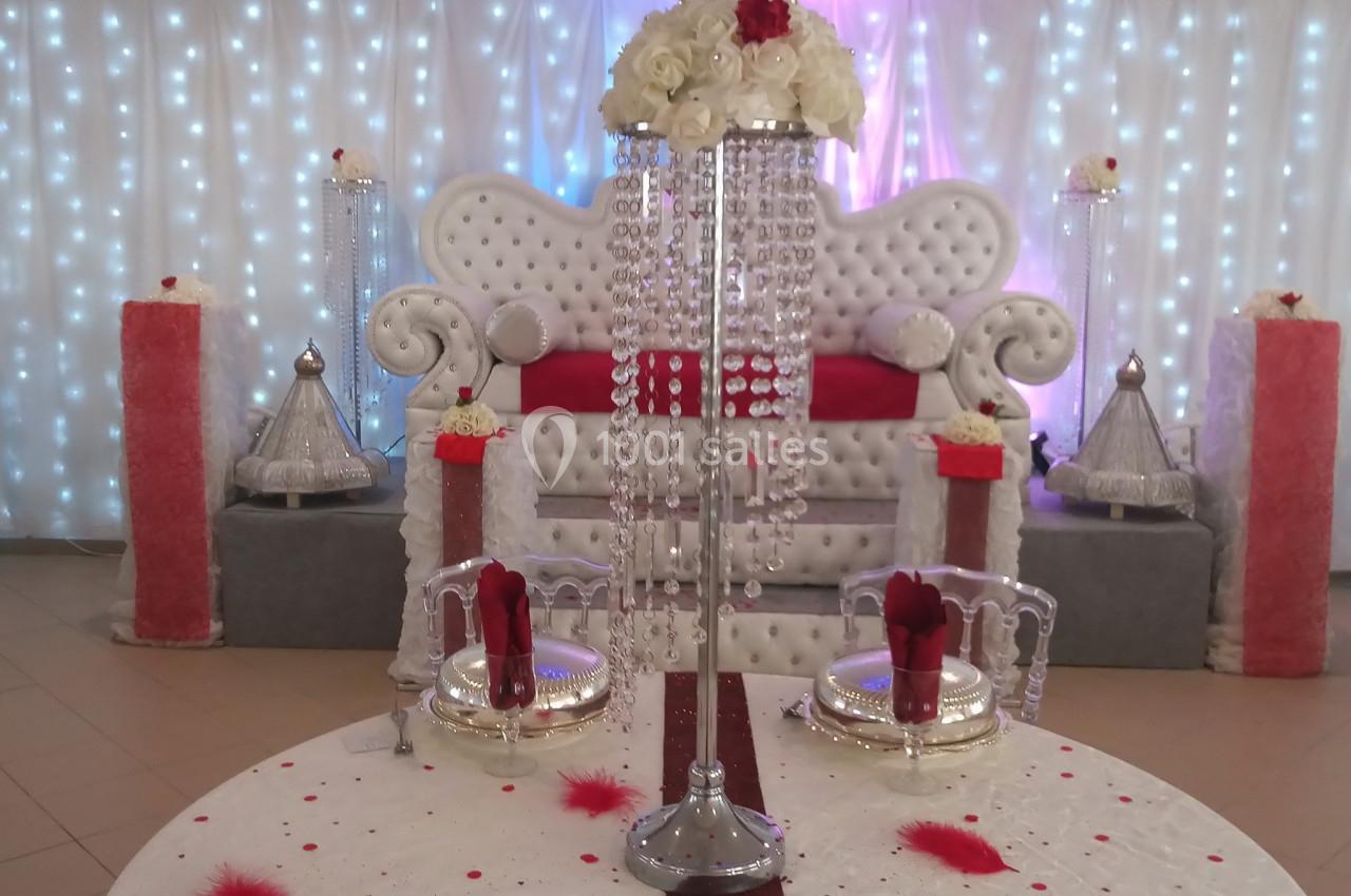 Décoration de mariage avec table ornée de fleurs, cristaux et bougies, devant un canapé capitonné et un fond lumineux.