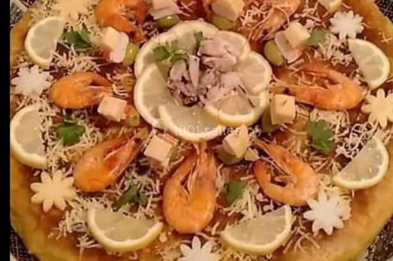 Grande galette garnie de crevettes, rondelles de citron, fromage, olives et décorations florales comestibles.