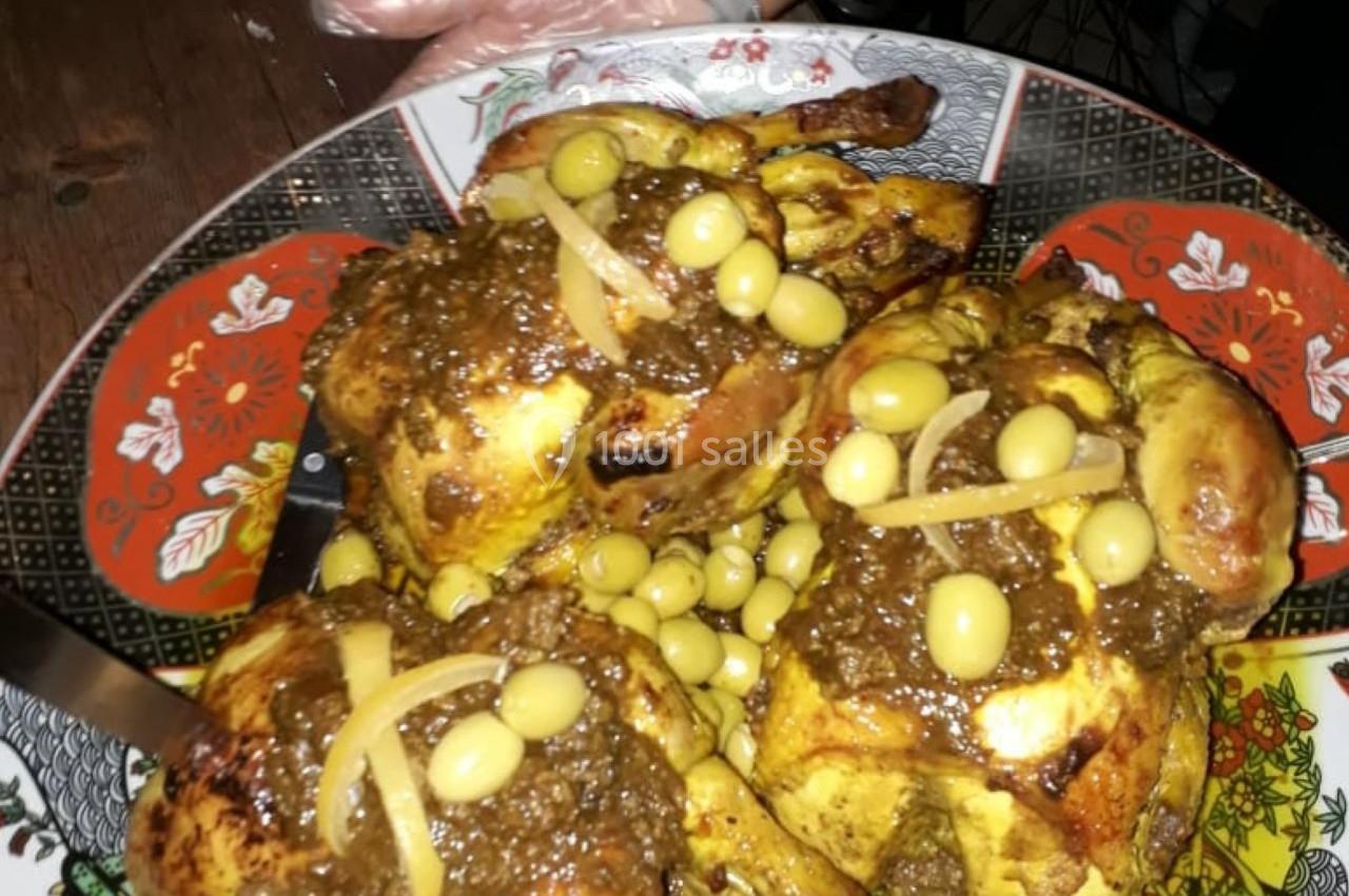 Poulet rôti garni d'olives et d'oignons, nappé de sauce épicée, présenté sur un plat décoratif.