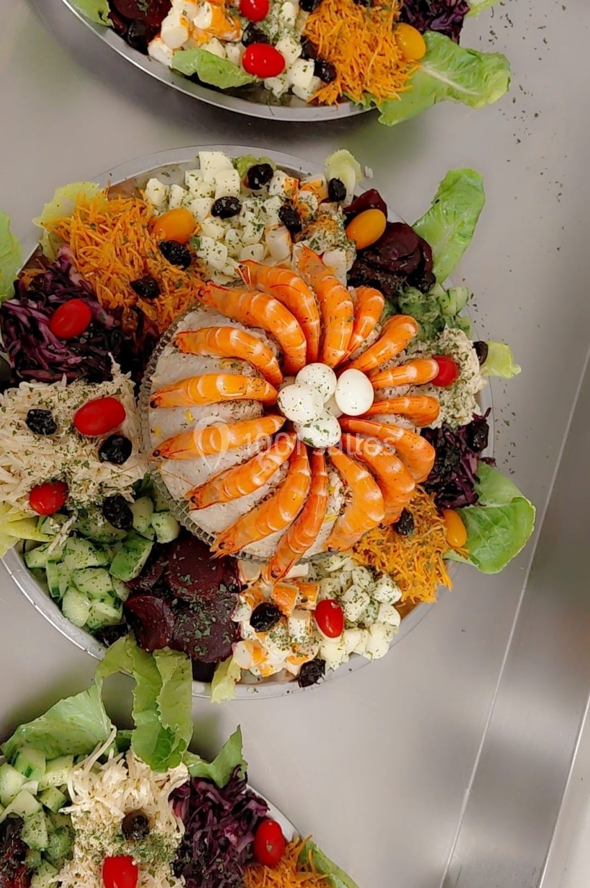 Assiette garnie de crevettes, légumes variés, œufs et olives, présentée avec soin sur un lit de salade.