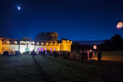 Château illuminé de nuit avec des murs en pierre, entouré d'arbres et d'une chaîne métallique au premier plan.