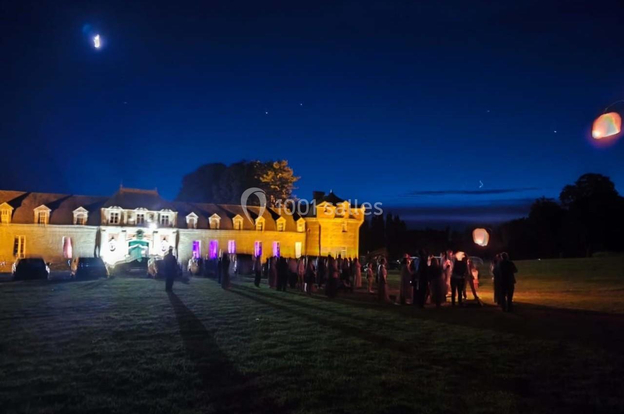 Groupe de personnes rassemblées devant un bâtiment illuminé la nuit, avec des lanternes flottant dans le ciel étoilé.