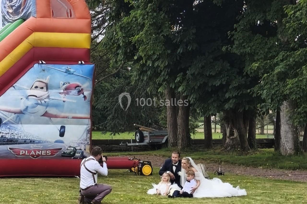 Un photographe capture une famille en tenue de mariage posant sur une pelouse près d'un château gonflable.