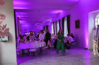 Château illuminé de nuit avec des murs en pierre, entouré d'arbres et d'une chaîne métallique au premier plan.