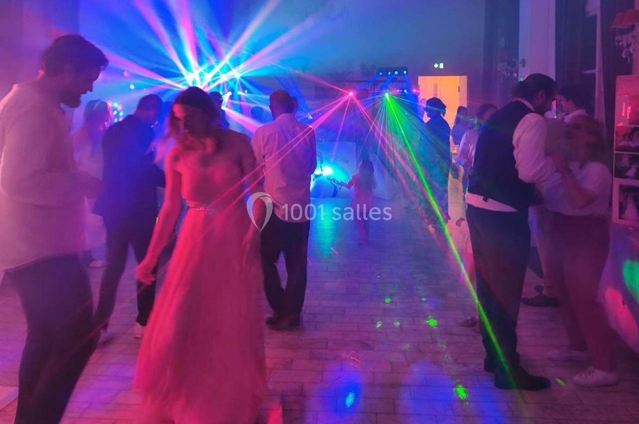 Personnes dansant sur une piste éclairée par des faisceaux lumineux colorés dans une ambiance festive.