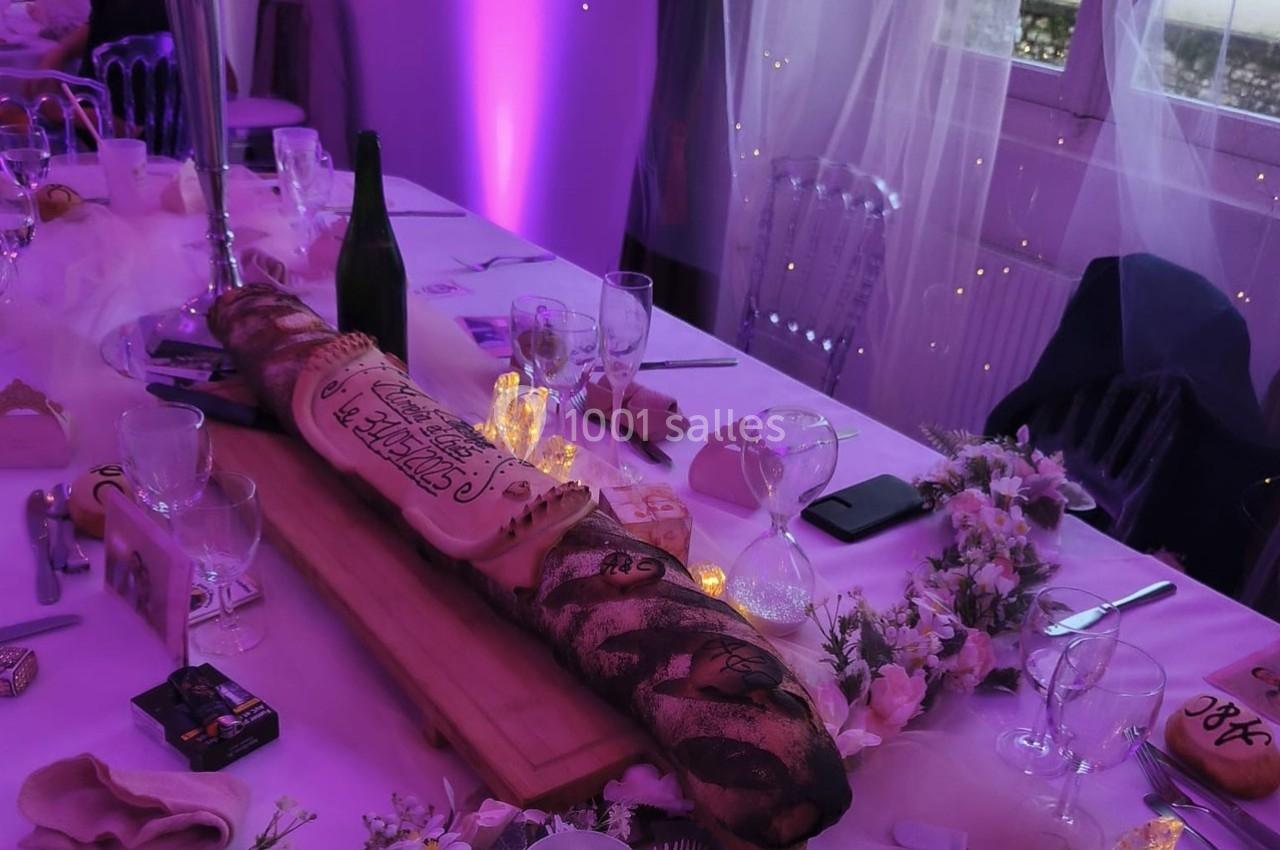 Table décorée pour un événement avec une longue baguette personnalisée, des fleurs, des bougies et des verres.