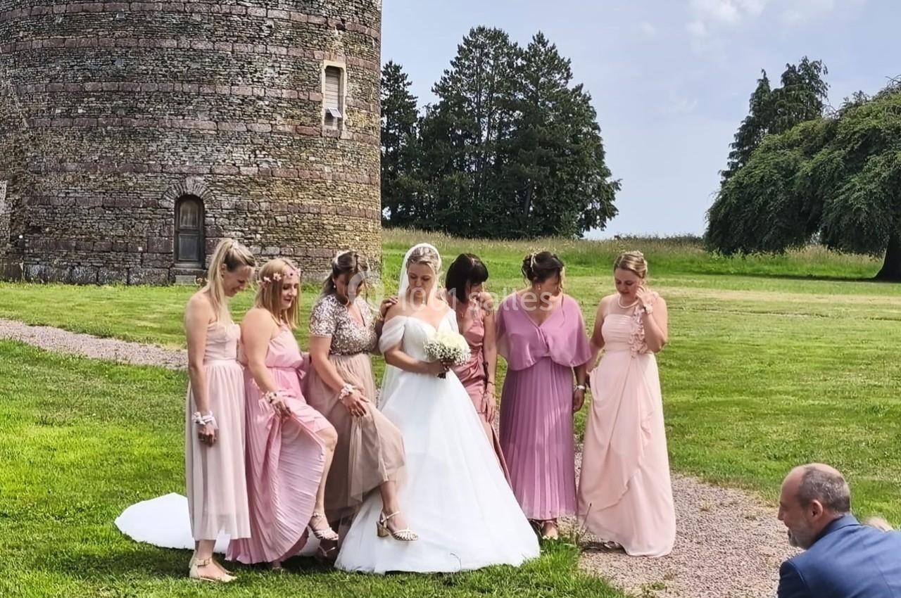 Une mariée en robe blanche pose avec ses demoiselles d'honneur en robes roses devant une tour en pierre et un espace vert.