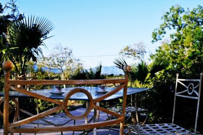 Table et chaises en fer forgé avec coussins bleus sur une terrasse ensoleillée devant un bâtiment en briques et grandes…