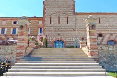 Table et chaises en fer forgé avec coussins bleus sur une terrasse ensoleillée devant un bâtiment en briques et grandes…