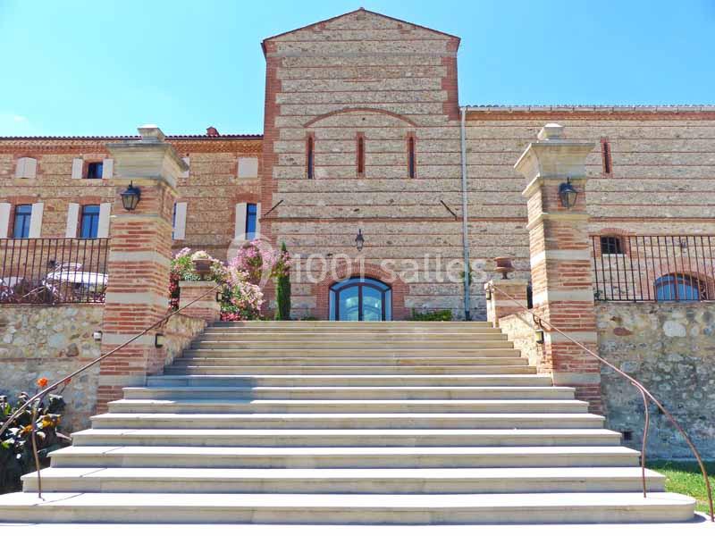 Escalier en pierre menant à un bâtiment en briques avec une façade symétrique et des colonnes décoratives.