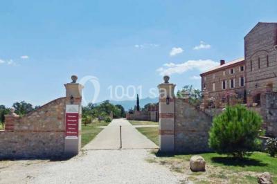 Table et chaises en fer forgé avec coussins bleus sur une terrasse ensoleillée devant un bâtiment en briques et grandes…