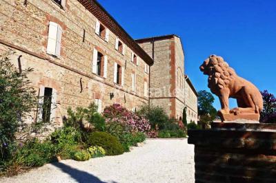 Table et chaises en fer forgé avec coussins bleus sur une terrasse ensoleillée devant un bâtiment en briques et grandes…