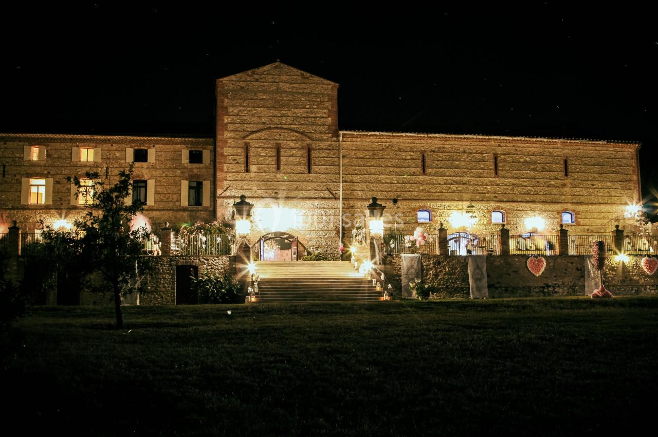 Façade d'un grand bâtiment en pierre éclairé la nuit, avec des escaliers et des lampadaires devant.