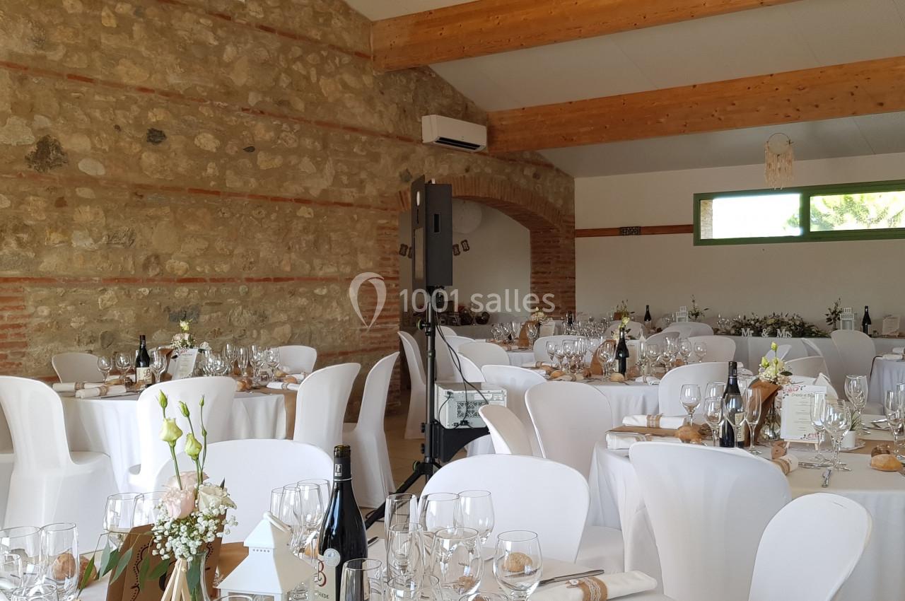 Salle de réception décorée avec des tables rondes dressées, nappes blanches et arrangements floraux.