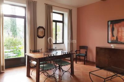 Table et chaises en fer forgé avec coussins bleus sur une terrasse ensoleillée devant un bâtiment en briques et grandes…