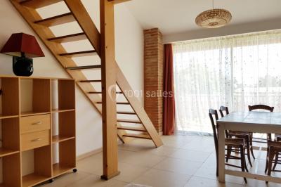 Table et chaises en fer forgé avec coussins bleus sur une terrasse ensoleillée devant un bâtiment en briques et grandes…