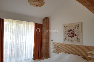 Table et chaises en fer forgé avec coussins bleus sur une terrasse ensoleillée devant un bâtiment en briques et grandes…
