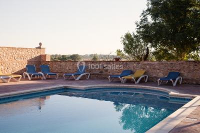 Table et chaises en fer forgé avec coussins bleus sur une terrasse ensoleillée devant un bâtiment en briques et grandes…