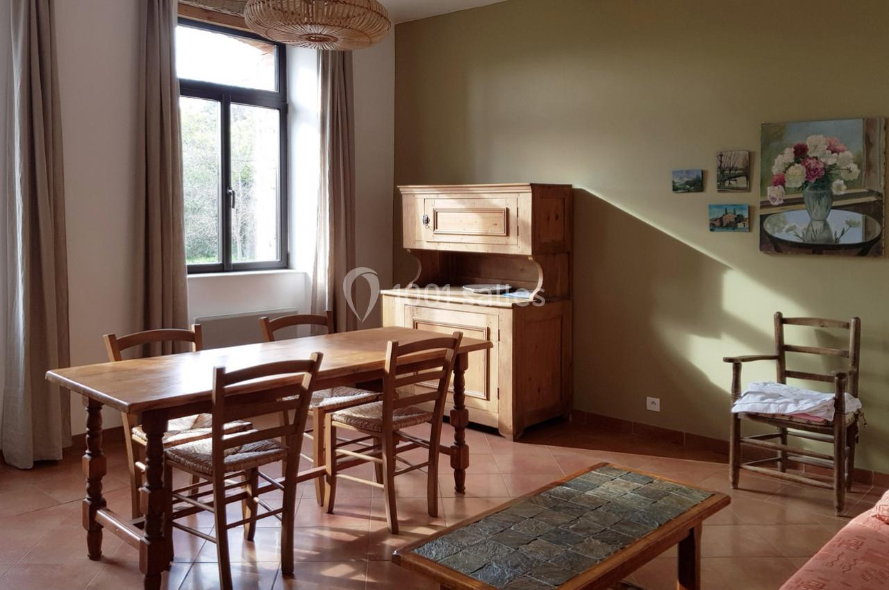 Salle à manger lumineuse avec table en bois, chaises assorties, buffet ancien et murs décorés de tableaux.