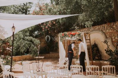 Table et chaises en fer forgé avec coussins bleus sur une terrasse ensoleillée devant un bâtiment en briques et grandes…