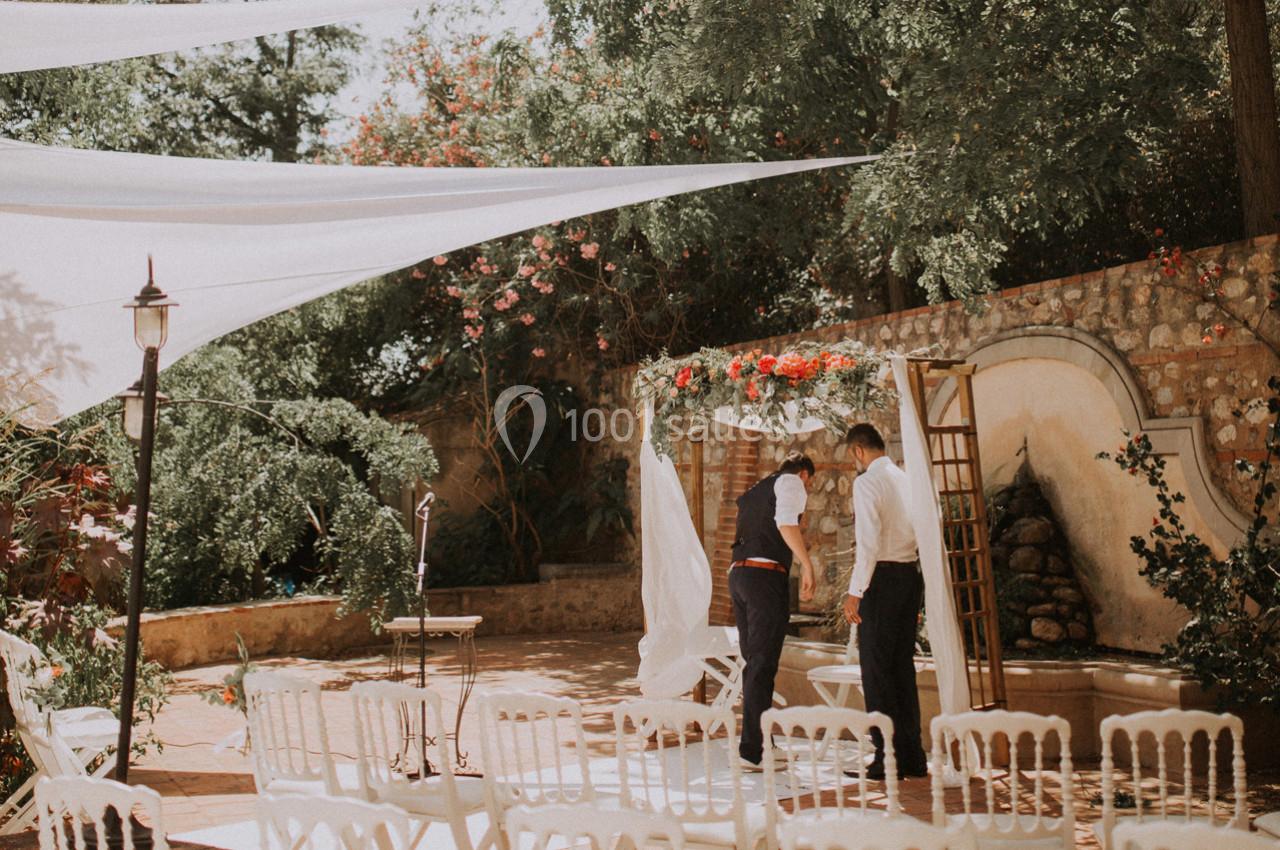 Deux hommes préparent une arche décorée de fleurs dans une cour extérieure aménagée pour une cérémonie.