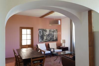 Table et chaises en fer forgé avec coussins bleus sur une terrasse ensoleillée devant un bâtiment en briques et grandes…