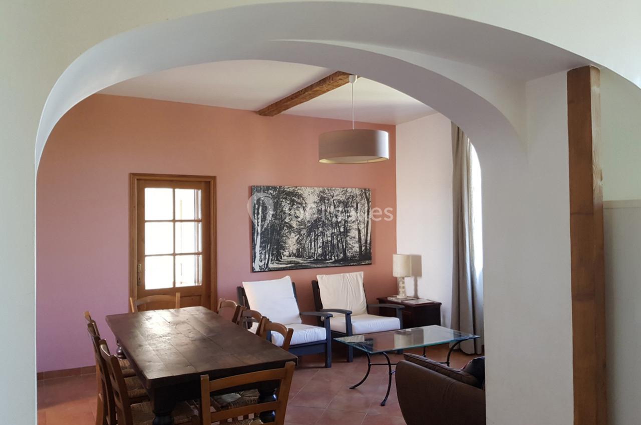 Salle à manger avec table en bois, chaises, coin salon, mur rose, tableau en noir et blanc et lampe suspendue.