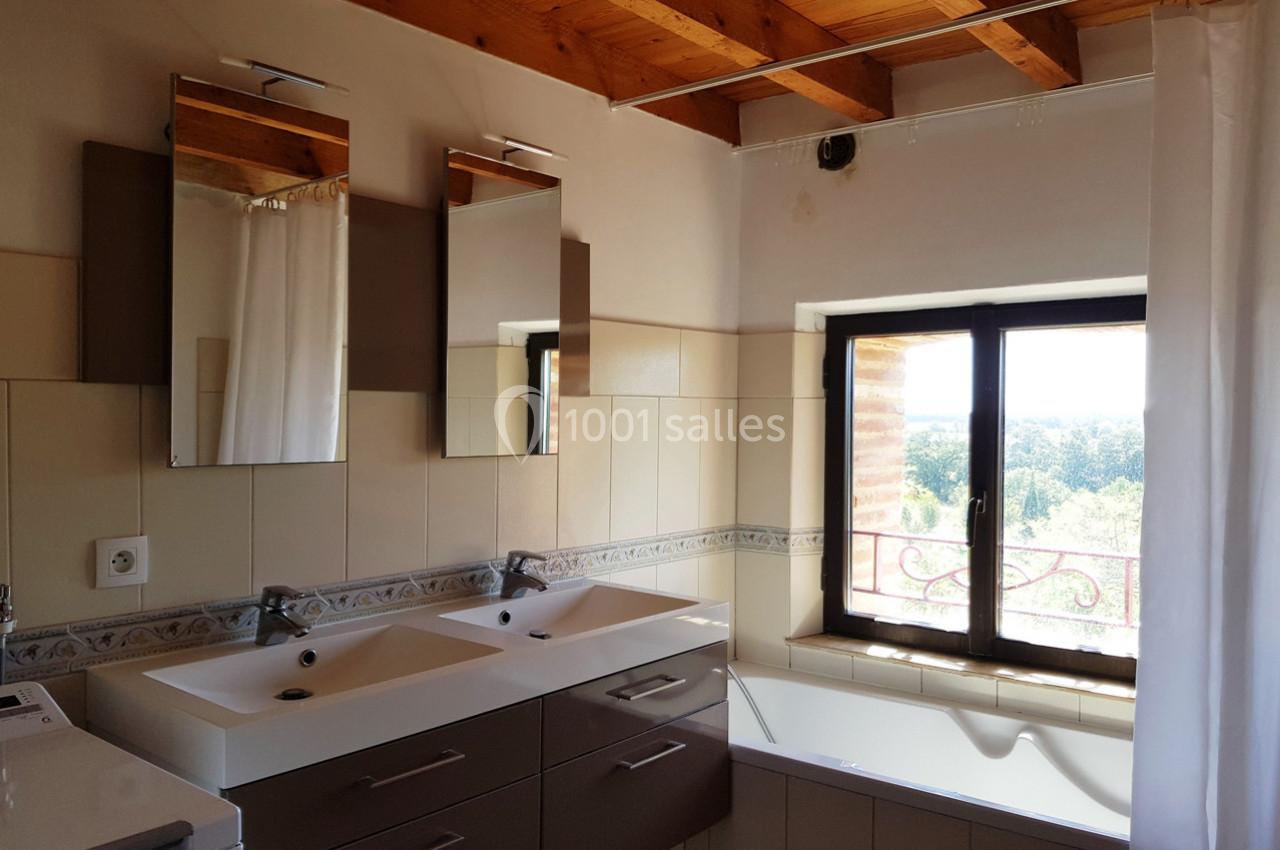 Salle de bain lumineuse avec double vasque, baignoire, miroir, et fenêtre donnant sur un paysage extérieur.