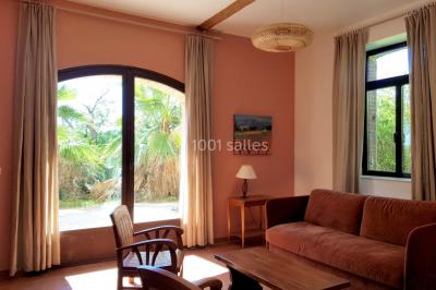 Table et chaises en fer forgé avec coussins bleus sur une terrasse ensoleillée devant un bâtiment en briques et grandes…