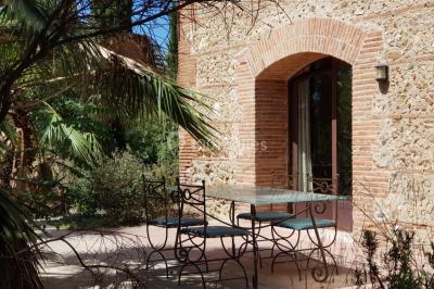Table et chaises en fer forgé avec coussins bleus sur une terrasse ensoleillée devant un bâtiment en briques et grandes…