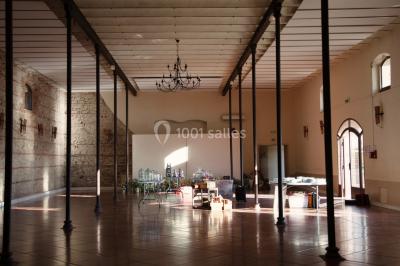 Table et chaises en fer forgé avec coussins bleus sur une terrasse ensoleillée devant un bâtiment en briques et grandes…