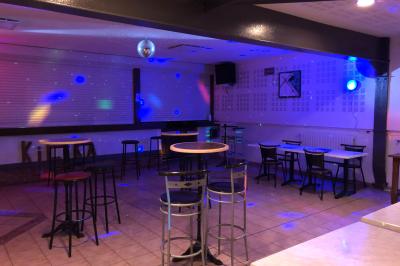 Bar avec comptoir en bois, tabourets, table ronde sur un tonneau, éclairage coloré et décoration murale.