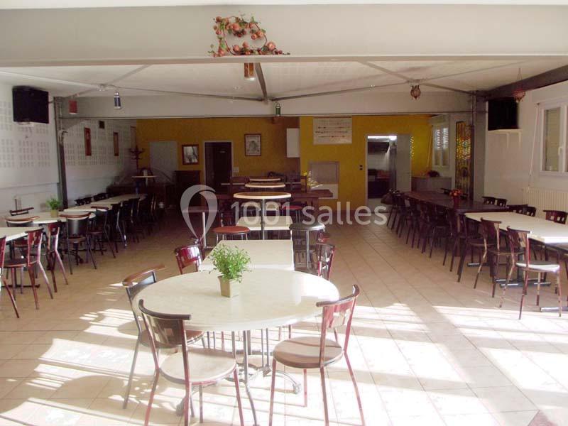 Salle lumineuse avec tables rondes et chaises disposées de manière espacée, décorations simples et murs clairs.