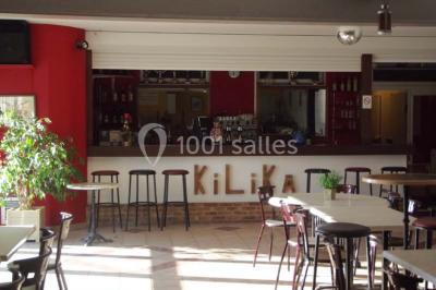 Bar avec comptoir en bois, tabourets, table ronde sur un tonneau, éclairage coloré et décoration murale.