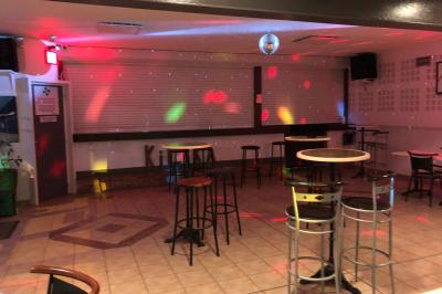 Bar avec comptoir en bois, tabourets, table ronde sur un tonneau, éclairage coloré et décoration murale.