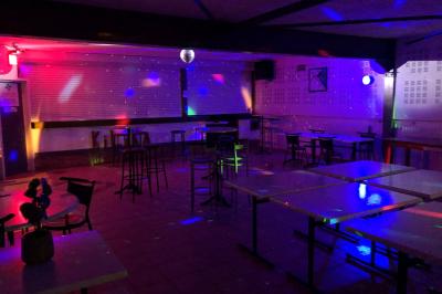 Bar avec comptoir en bois, tabourets, table ronde sur un tonneau, éclairage coloré et décoration murale.