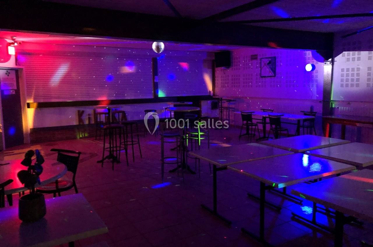 Salle vide avec tables et chaises, éclairée par des lumières colorées et des spots, ambiance de fête ou de soirée.