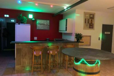 Bar avec comptoir en bois, tabourets, table ronde sur un tonneau, éclairage coloré et décoration murale.