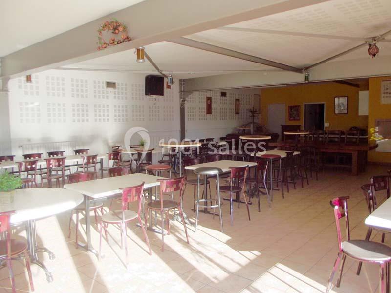 Salle lumineuse avec tables et chaises disposées de manière espacée, murs clairs et décorations murales simples.
