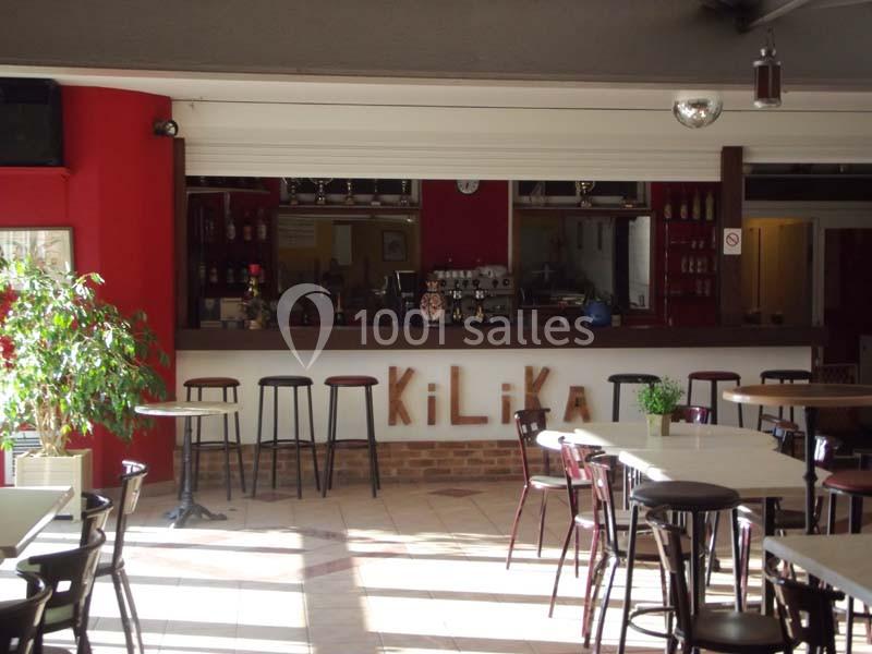 Bar intérieur avec comptoir en bois, tabourets hauts, tables et chaises, décoré de murs rouges et d'une plante verte.