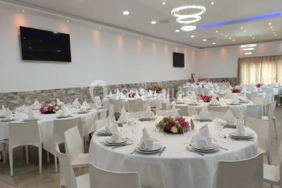 Bâtiment à façade rouge et blanche avec une pergola blanche et un banc en pierre dans un jardin verdoyant.