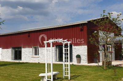 Bâtiment à façade rouge et blanche avec une pergola blanche et un banc en pierre dans un jardin verdoyant.