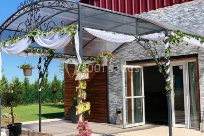 Bâtiment à façade rouge et blanche avec une pergola blanche et un banc en pierre dans un jardin verdoyant.