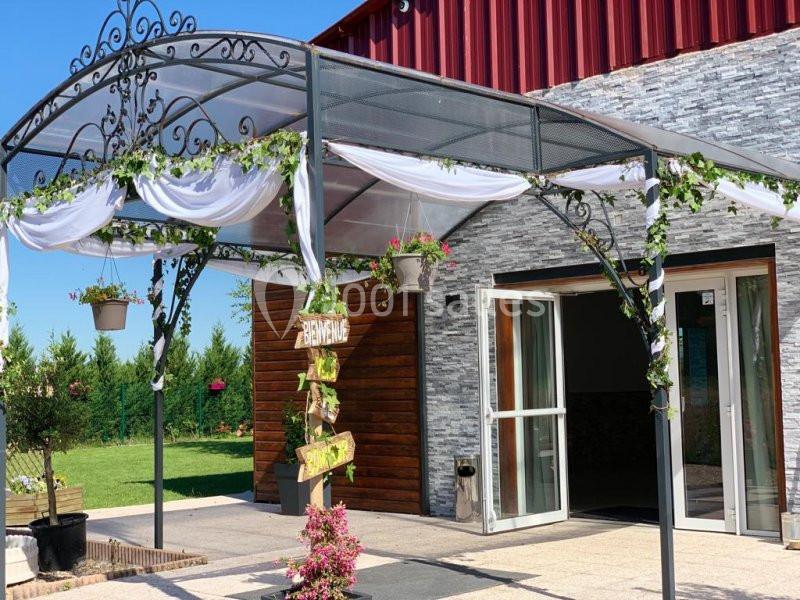 Entrée décorée avec une arche en fer forgé ornée de voilages blancs, de feuillages et de pots suspendus.