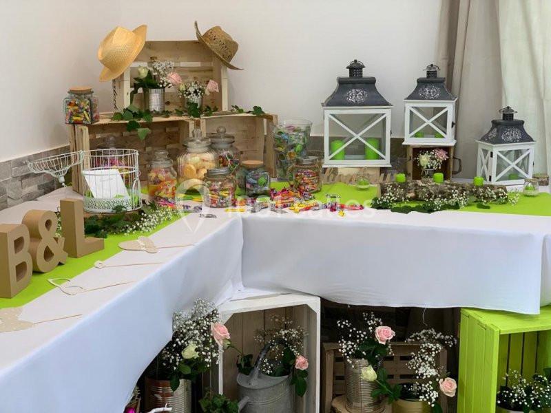 Table décorée pour une fête avec bonbonnières, lanternes, fleurs et lettres en bois sur une nappe blanche.