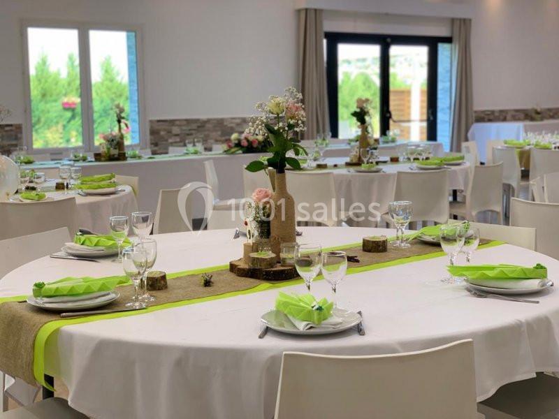 Salle de réception décorée avec des tables rondes, nappes blanches, chemins de table verts et centres de table floraux.