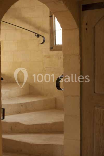 Escalier en pierre beige avec une rampe en métal noir, éclairé par une fenêtre et encadré par une arche.