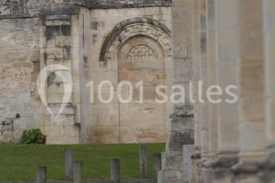 Un bâtiment en pierre avec un toit en tuiles rouges, entouré de jardins fleuris, accueille un groupe de personnes.
