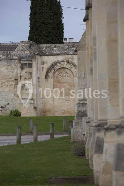 Mur en pierre avec une arche sculptée, entouré de pelouse et de colonnes d'un bâtiment adjacent.